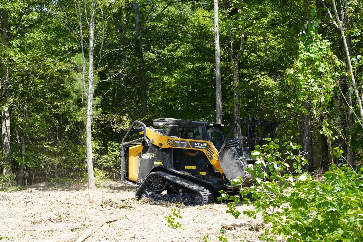 Clear Path mulcher paused at the edge of a freshly cleared area with dense green canopy behind, showing before-and-after contrast on a Middle Tennessee property