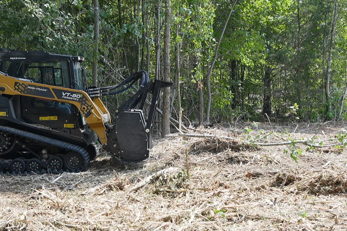 Wide view of freshly mulched ground cover extending across a cleared Tennessee property with the mulcher working at the tree line in the background